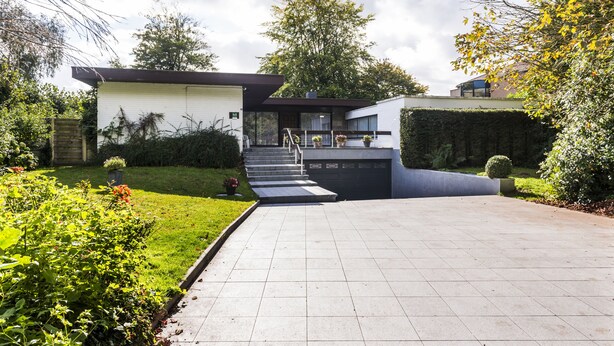 Une maison moderne avec une allée pavée, un jardin devant la maison agrémenté de verdure et un escalier menant à l’entrée.