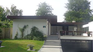 Une maison moderne à deux étages, dotée d’un jardin à l’avant, d’un garage et d’un escalier menant à l’entrée.