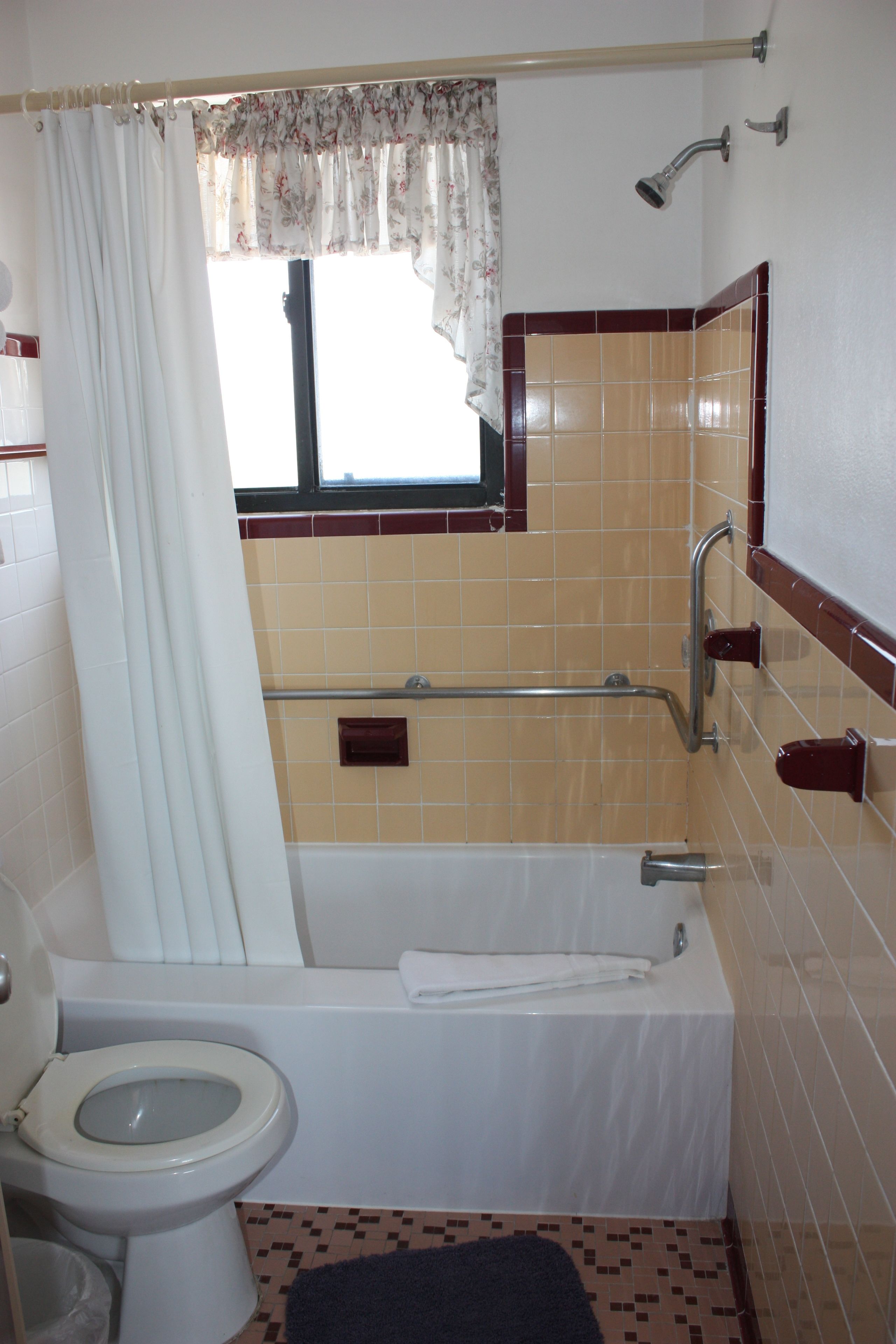 A bathroom with a toilet, bathtub, shower, and a window with a curtain.