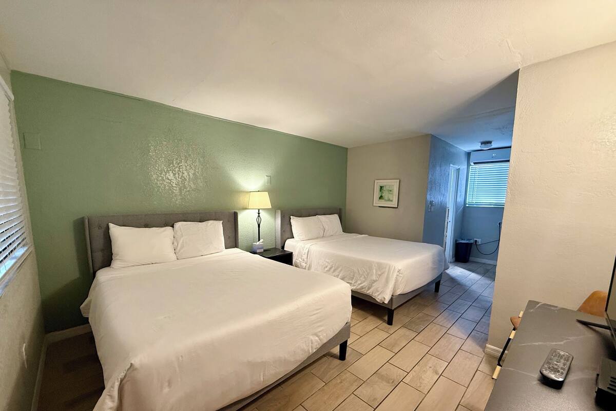 A hotel room with two beds, a desk, a lamp, and a picture on the wall.