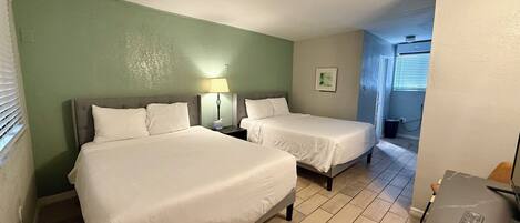 A hotel room with two beds, a desk, a lamp, and a picture on the wall.