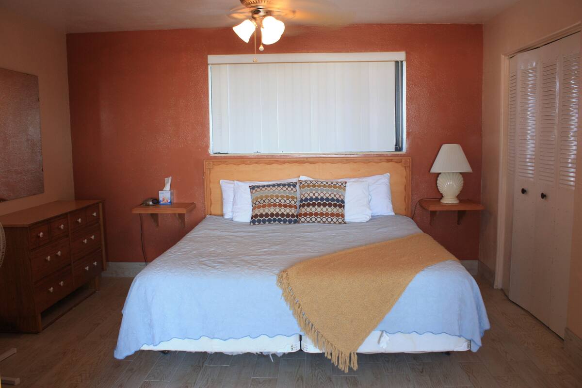 A bedroom with a bed, a nightstand, a lamp, a dresser, and a door.