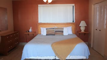 Quarto com cama, mesa de cabeceira, luminária, cômoda e porta.
