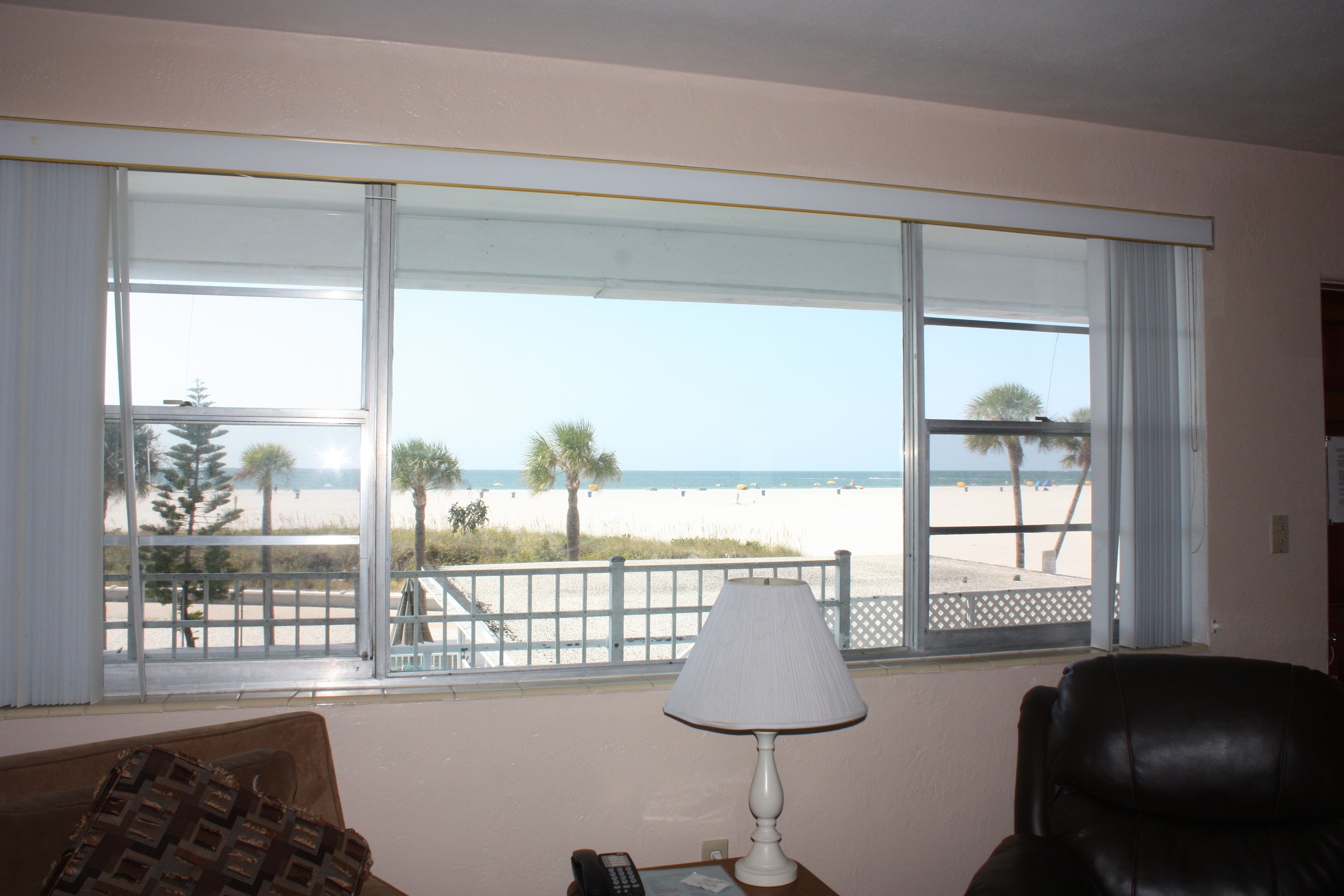 A room with a large window overlooking a beach, a lamp, and a leather chair.