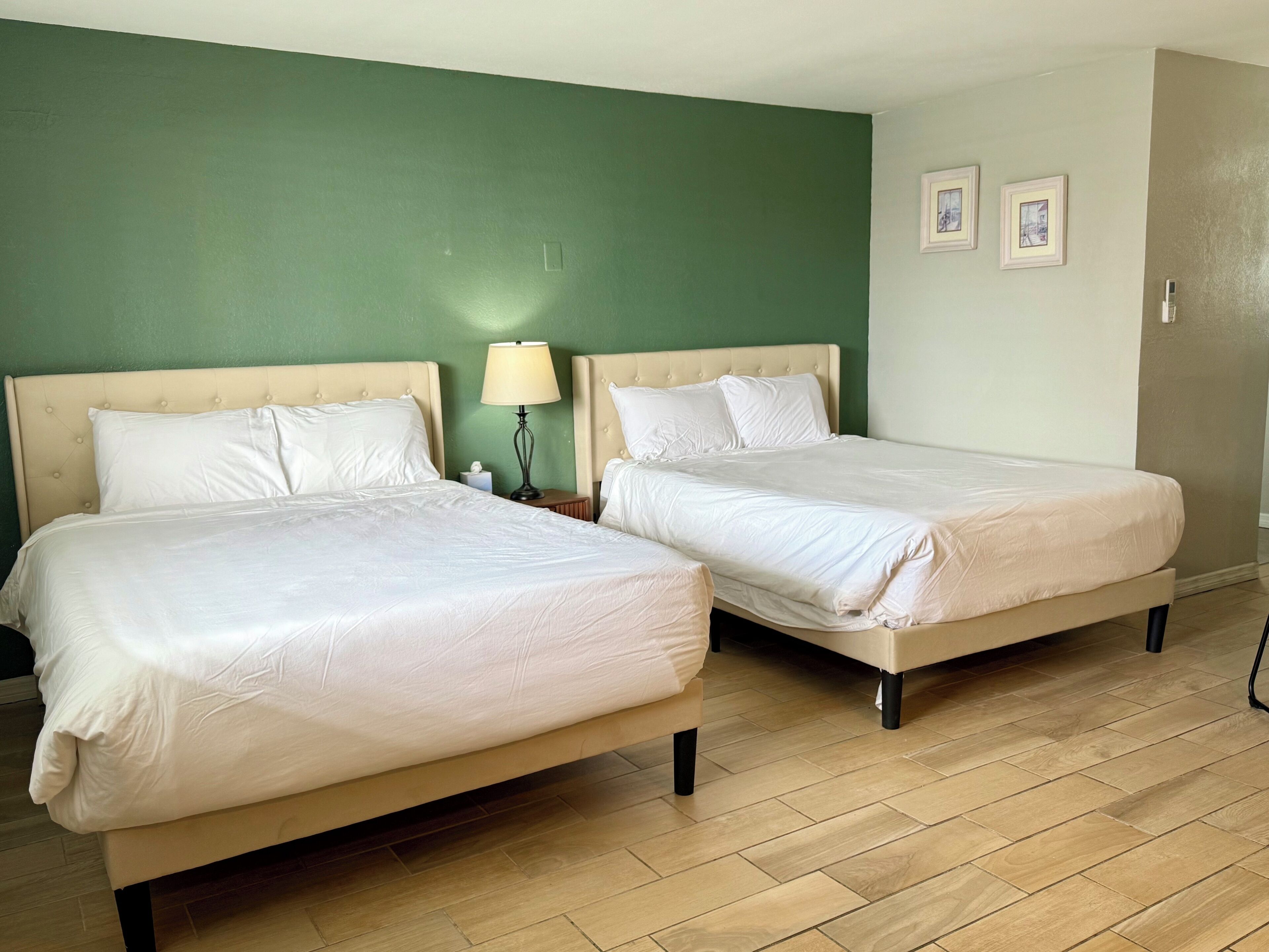 Zwei Einzelbetten mit weißer Bettwäsche in einem Zimmer mit grünen Wänden und Holzboden.