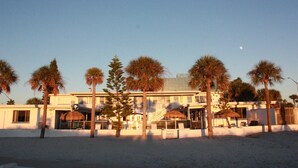 A beachfront hotel with palm trees, a thatched-roof structure, and a clear sky. - iBeach Resort (Treasure Island)