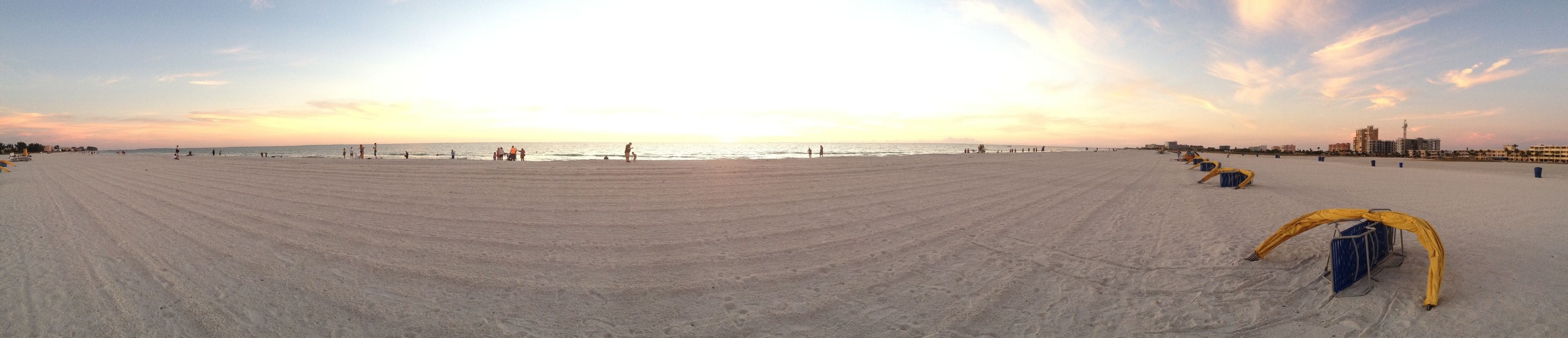 Une vaste plage de sable, avec un coucher de soleil en arrière-plan et quelques tentes installées sur la droite.
