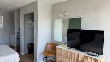 Une chambre d’hôtel avec un lit, un téléviseur posé sur une commode, une chaise et un dressing.