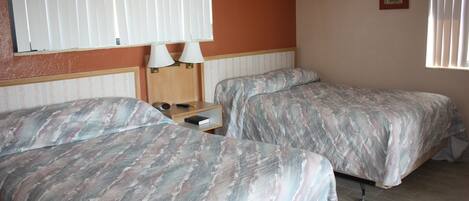 A bedroom with two beds, a nightstand, and a window with blinds.