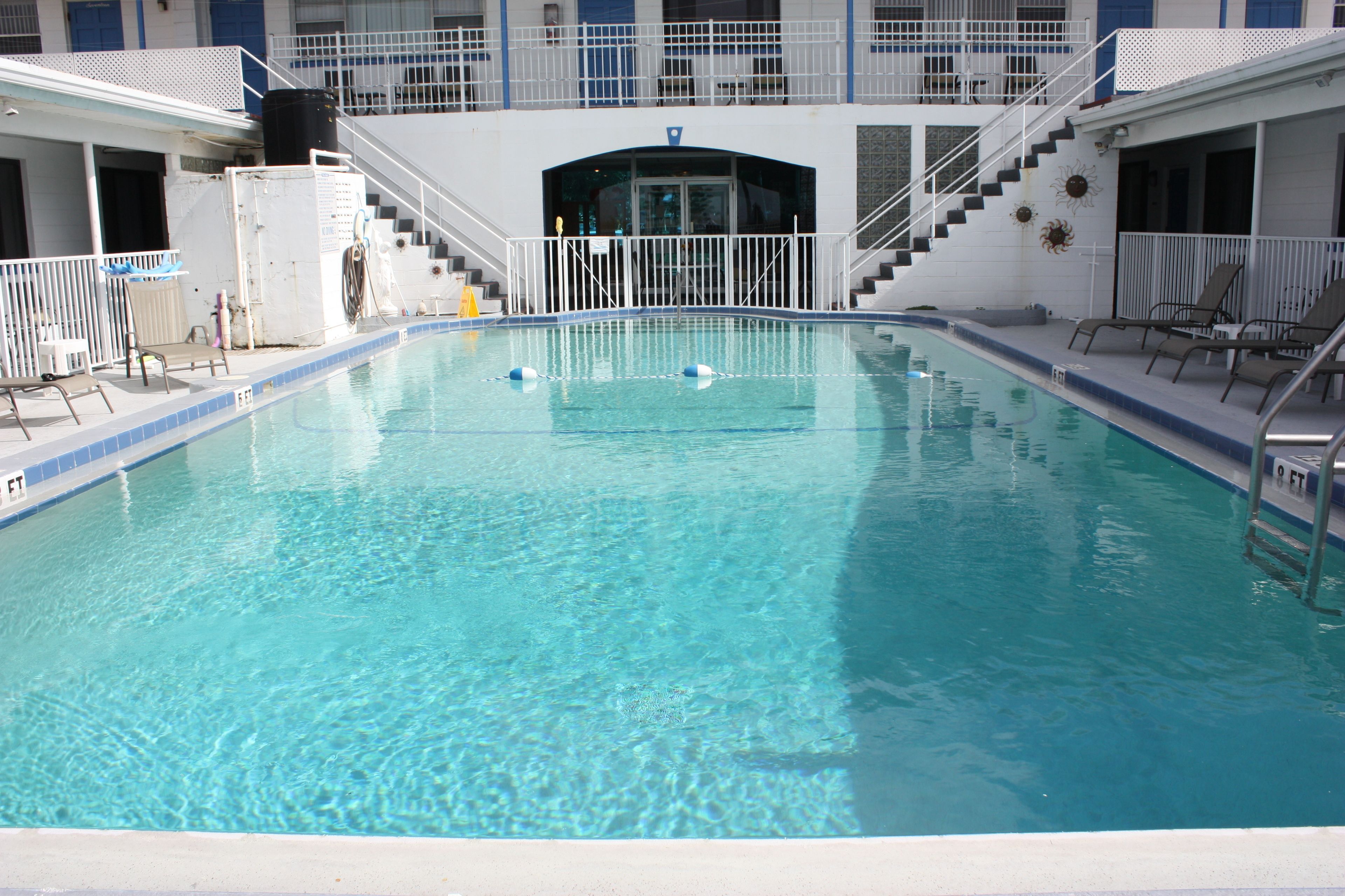 Une piscine rectangulaire à l’eau d’un bleu cristallin, entourée de rampes et de marches blanches menant à une entrée.