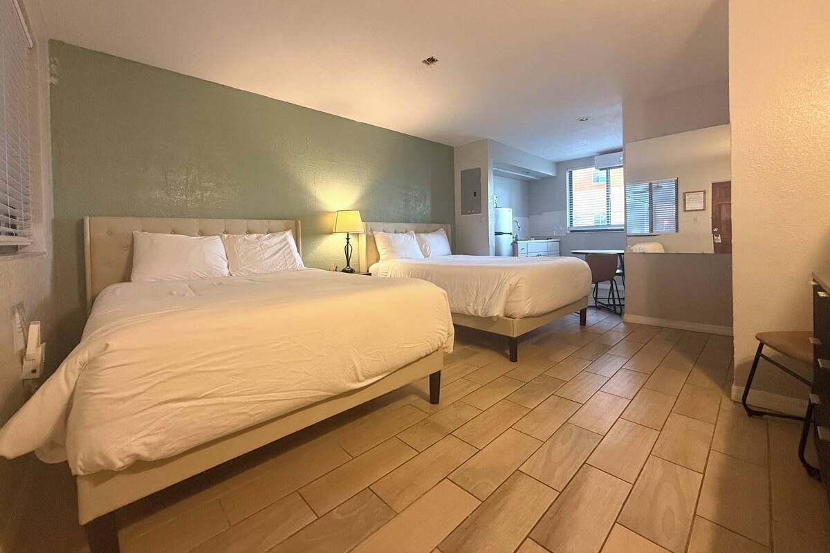 A hotel room with two beds, a desk, and a kitchenette.