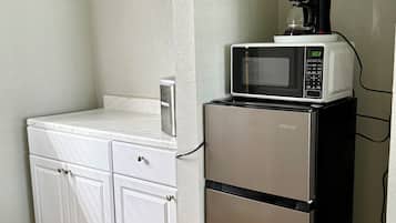 A compact kitchen with a stainless steel refrigerator, a microwave, and a coffee maker on top.