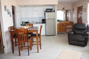 A compact kitchen with white cabinets, a stainless steel refrigerator, and a microwave. There is a dining table with chairs and a leather armchair. - iBeach Resort (Treasure Island)