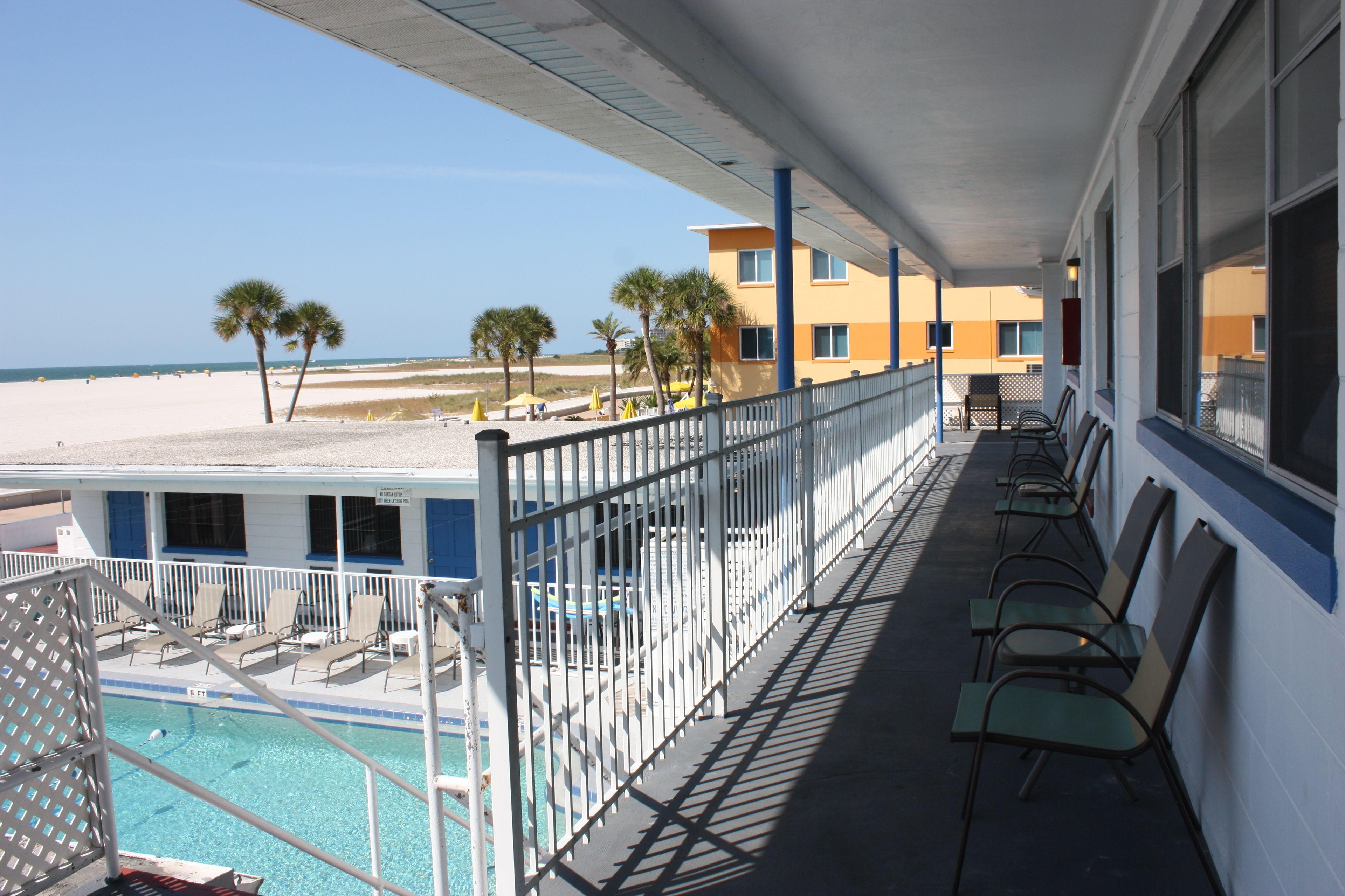 A balcony with a view of the beach and ocean, a pool, and several chairs and tables.