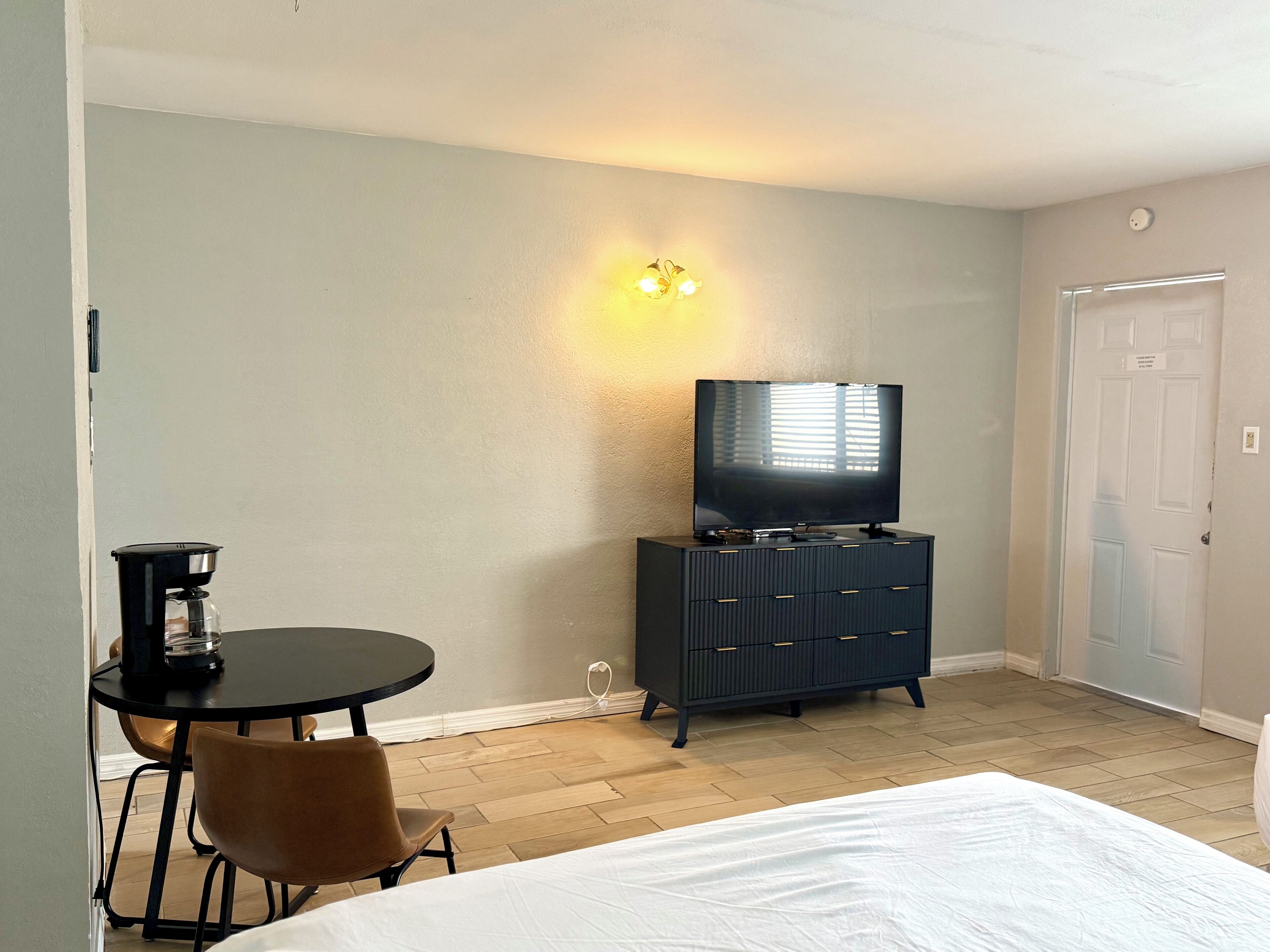 A hotel room with a bed, a television on a dresser, a coffee maker, and a chair.