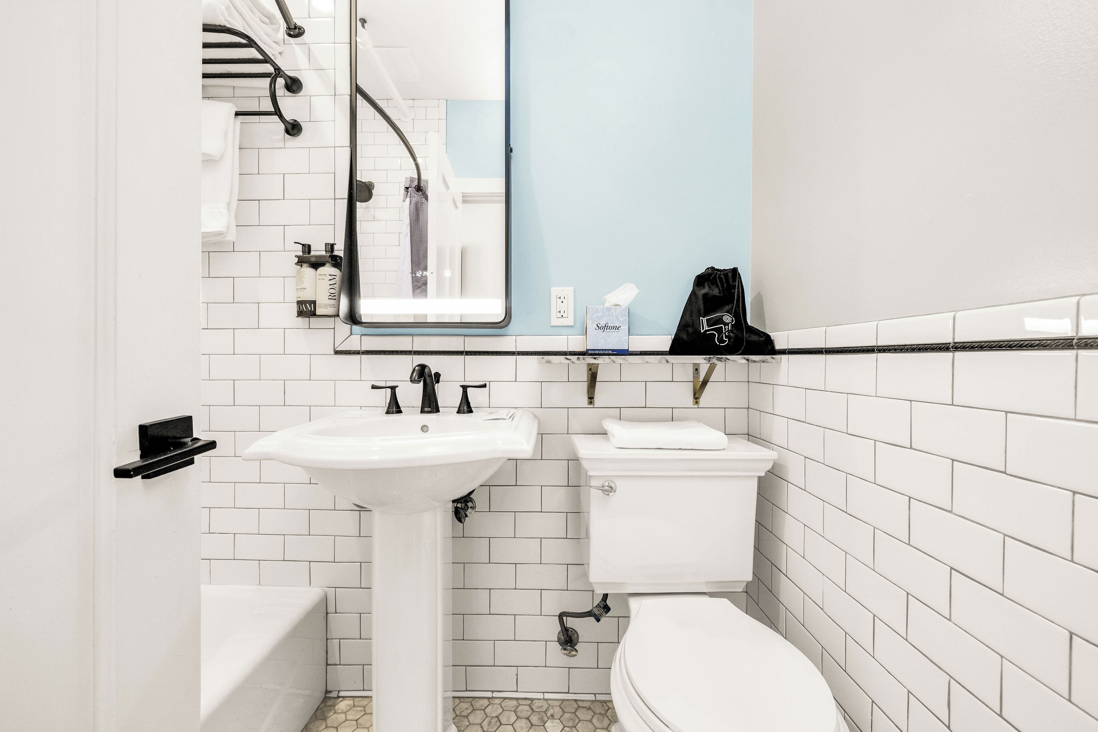 Une salle de bain avec un lavabo, des toilettes et une baignoire, tous de couleur blanche. Un miroir est placé au-dessus du lavabo, et un porte-serviettes contient des serviettes.