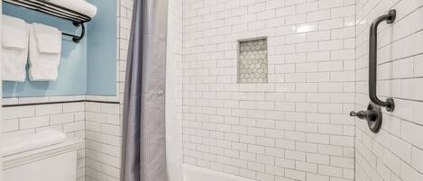 Un baño con paredes de azulejos blancos, una pared de acento azul, un inodoro blanco, una bañera y una cortina de ducha.