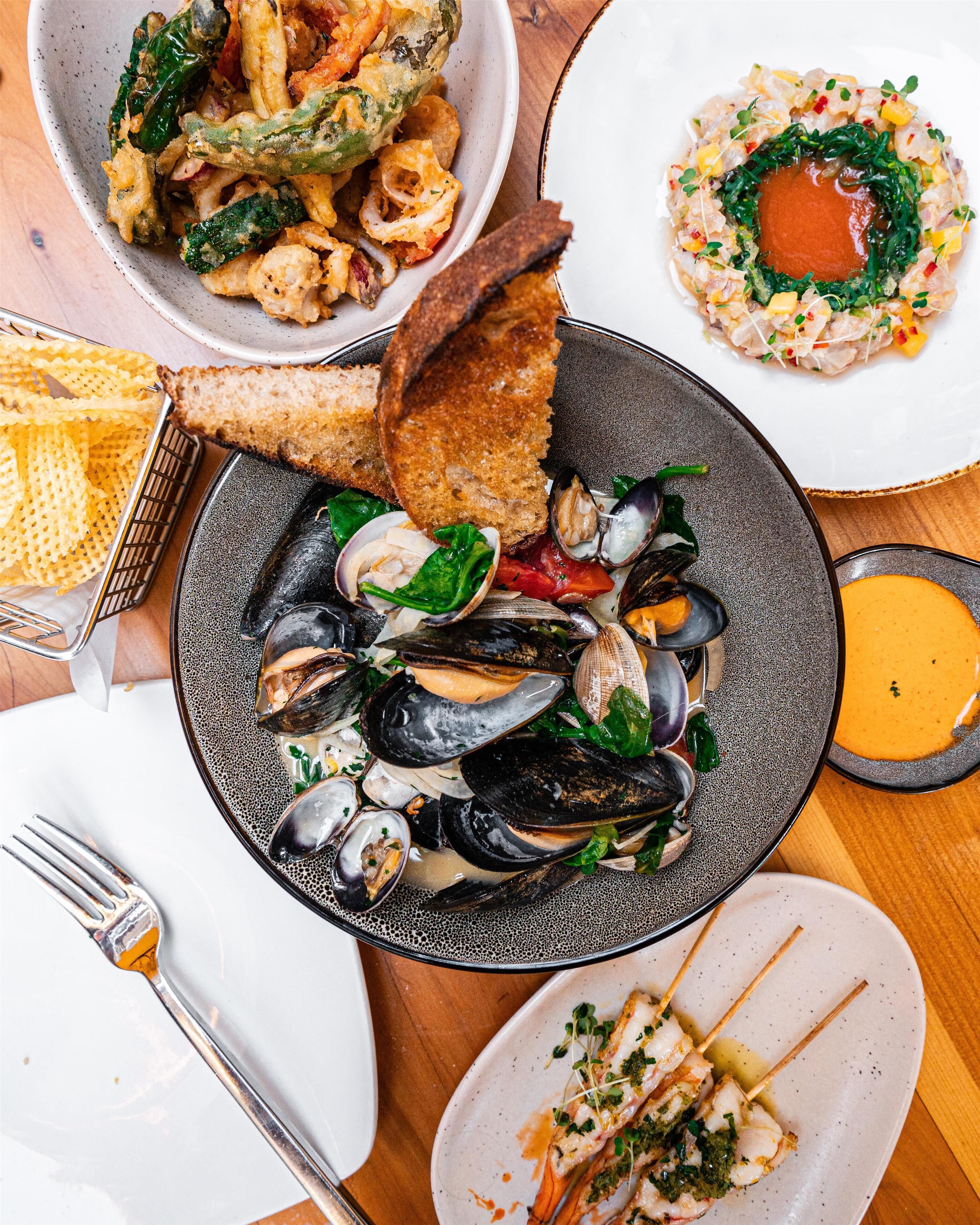 A variety of seafood dishes including mussels, shrimp, and squid, served on different plates.