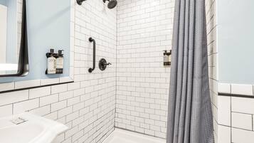 Un área de ducha con paredes de azulejos blancos, un cabezal de ducha negro y una cortina de ducha gris.