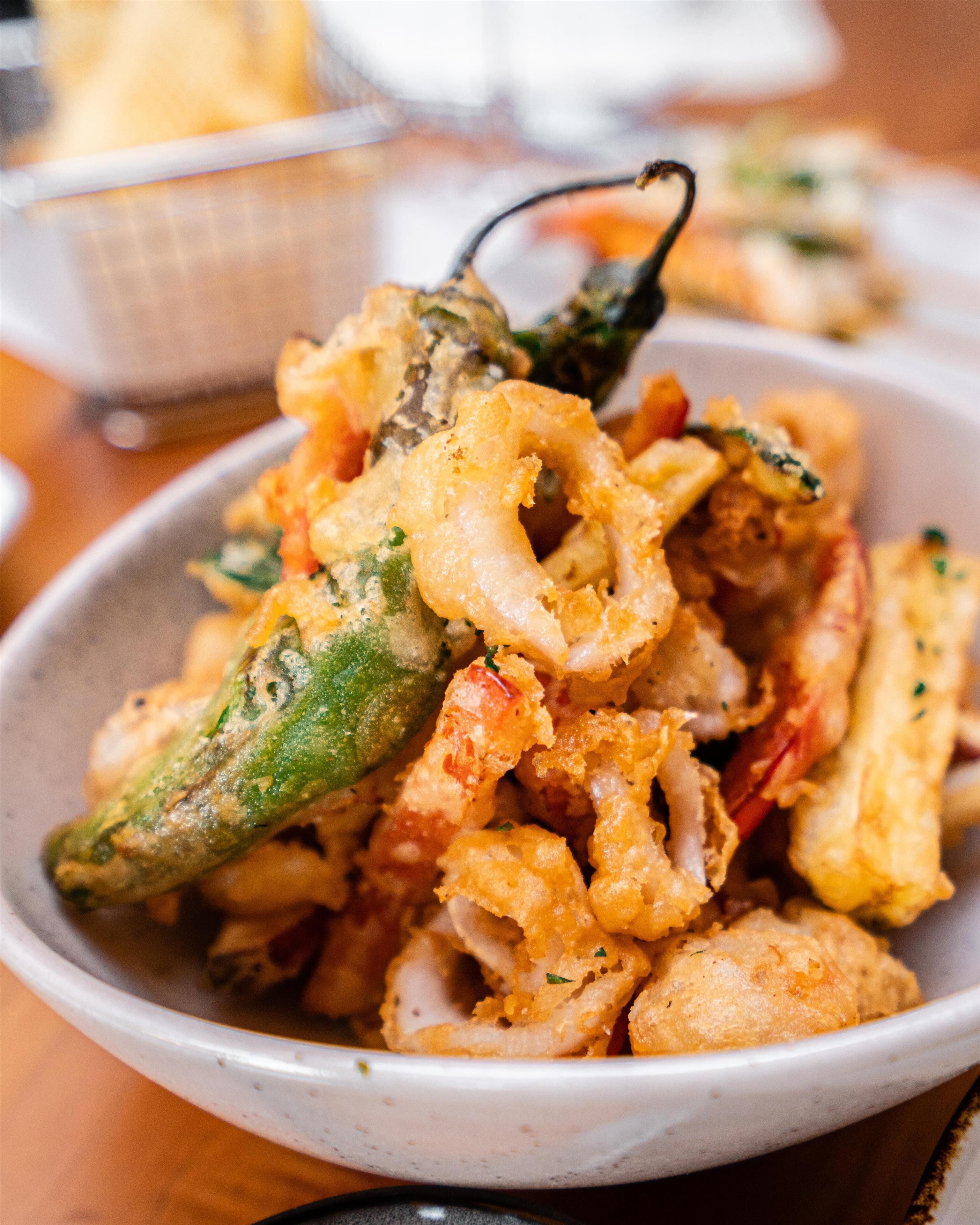 A bowl of fried seafood, including shrimp and squid, with a green chili visible.