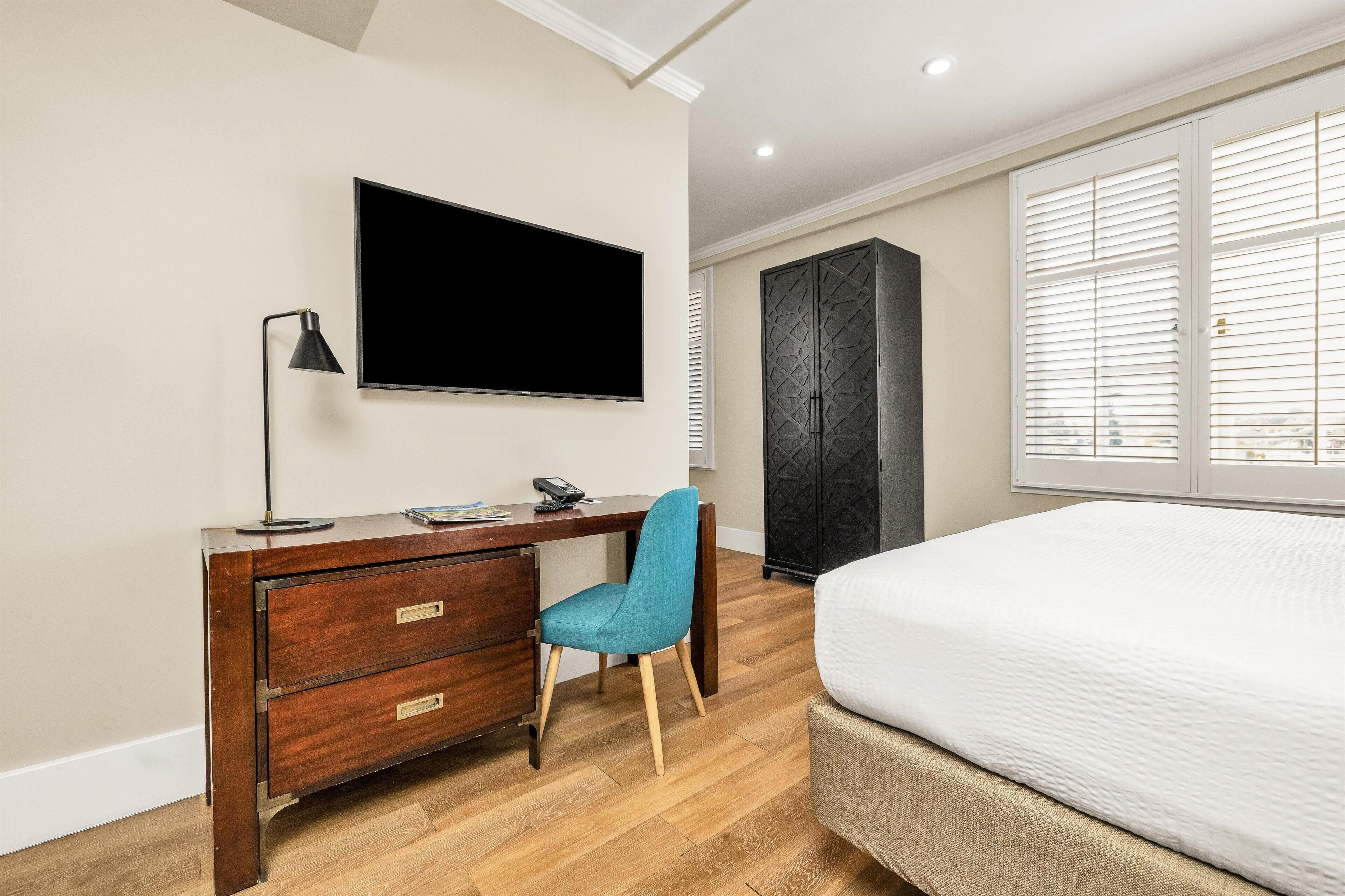 Una camera da letto con un letto, una scrivania con sedia, una TV e un armadio.