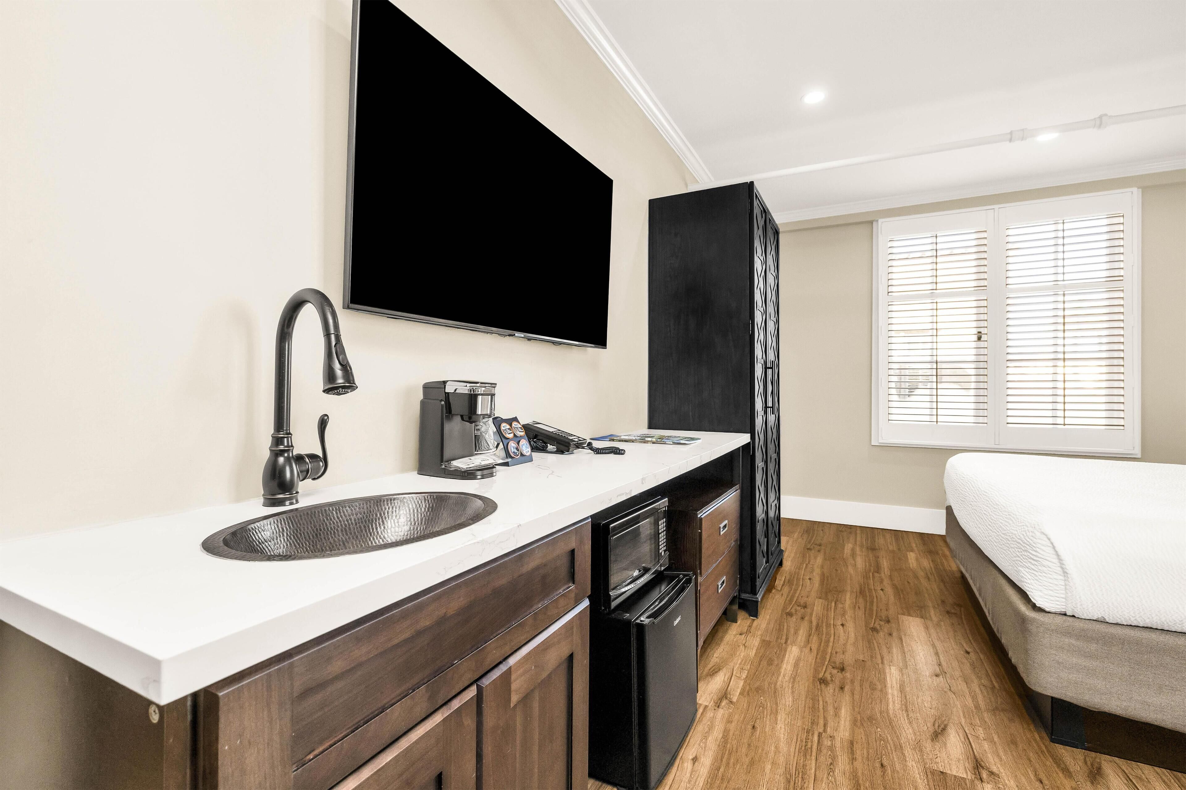 A modern bathroom with a sink, mirror, and a flat-screen TV mounted above it.