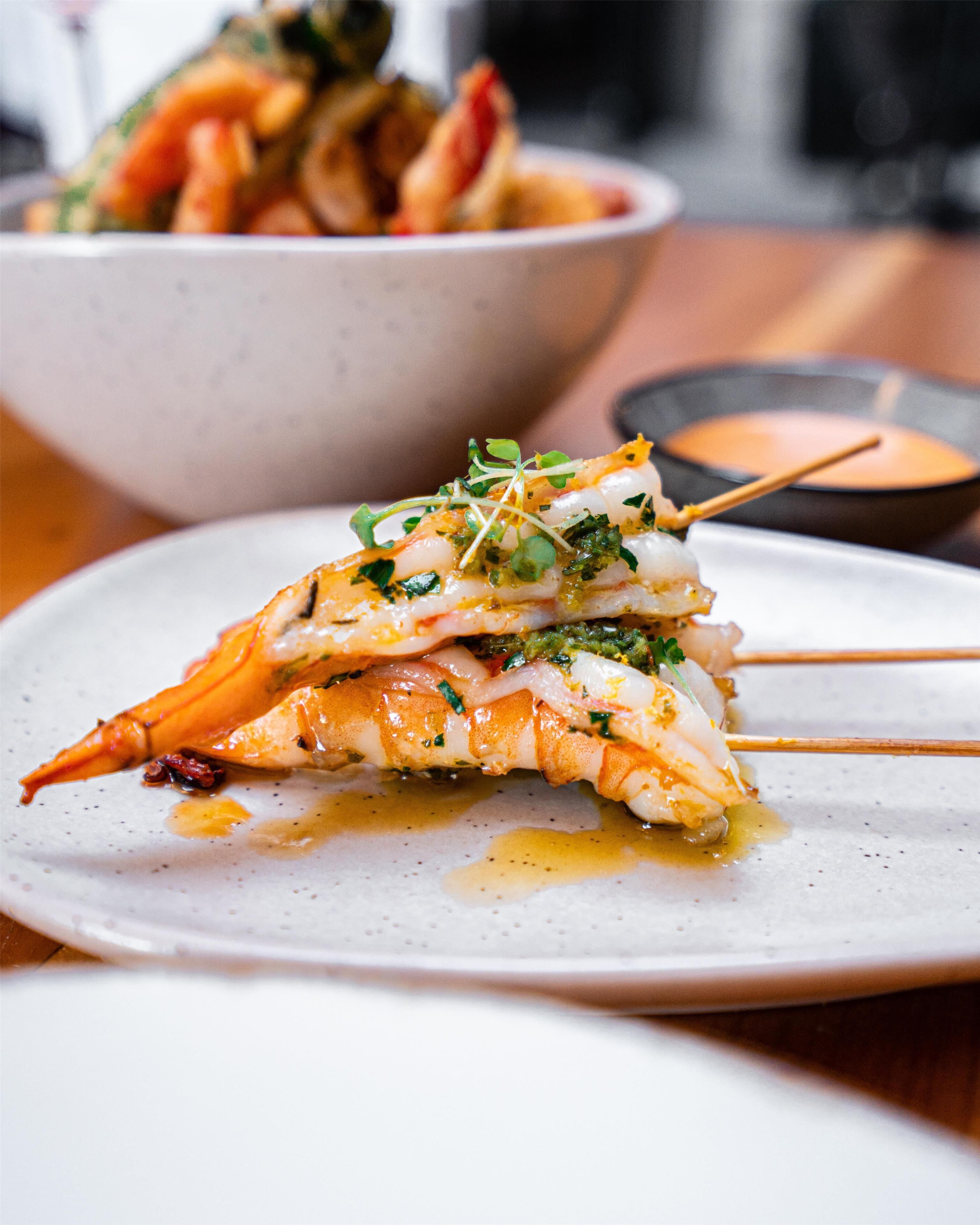 A plate of food with a seafood dish, a bowl in the background, and a small dish with sauce.