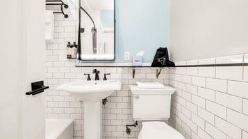 Une salle de bain avec un lavabo, des toilettes et une baignoire, tous de couleur blanche. On trouve un porte-serviettes au-dessus du lavabo et un miroir sur le mur.