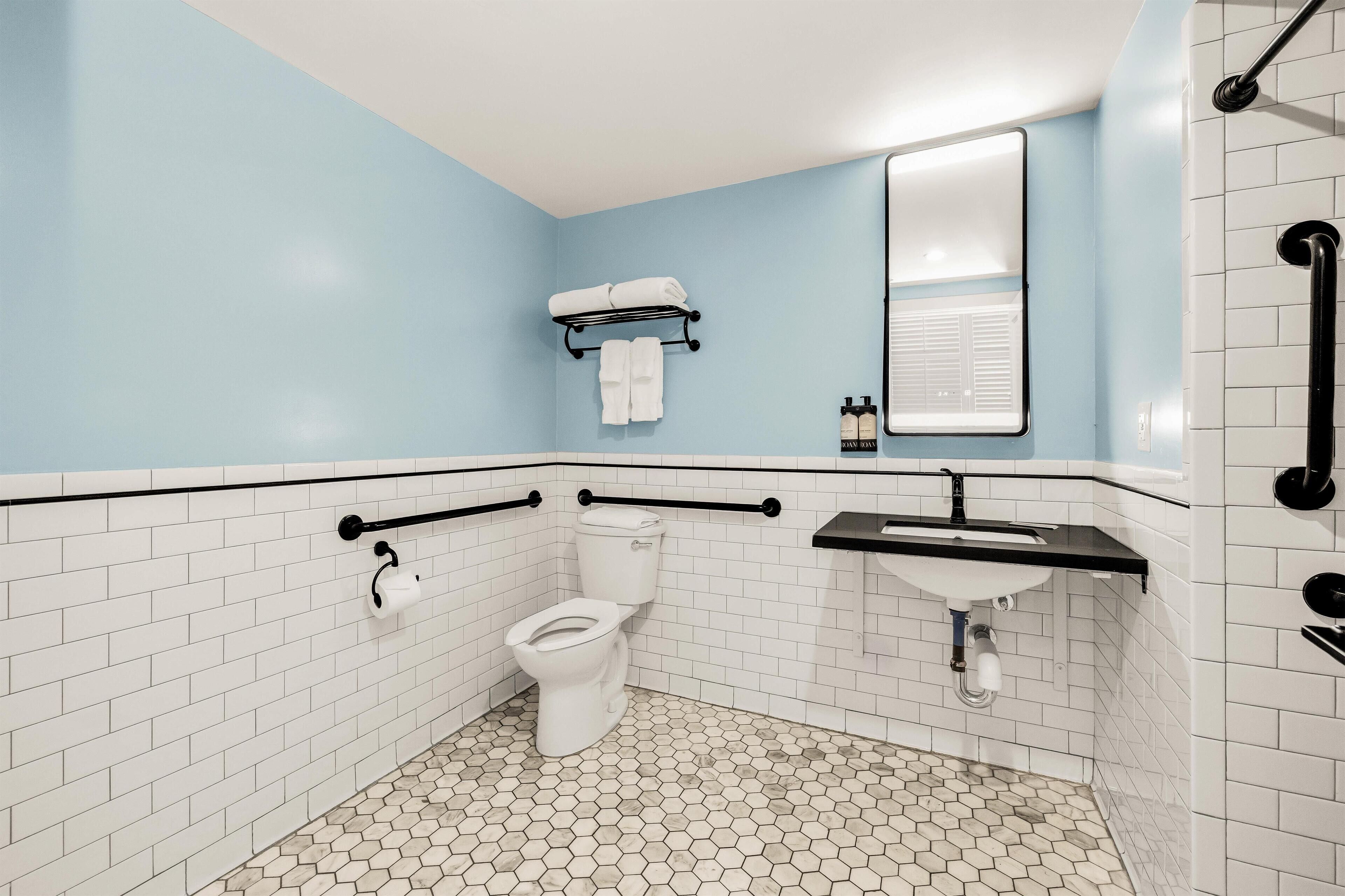 A bathroom with a white toilet, a sink, and a mirror. There are two towels hanging on a rack above the toilet.