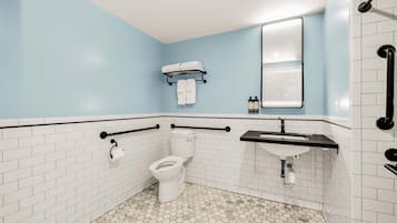 A bathroom with a white toilet, a sink, and a mirror. There are two towels hanging on a rack above the toilet.