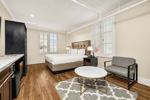 Un dormitorio con cama, mesita de noche, lámpara, silla y una pequeña mesa con alfombra.