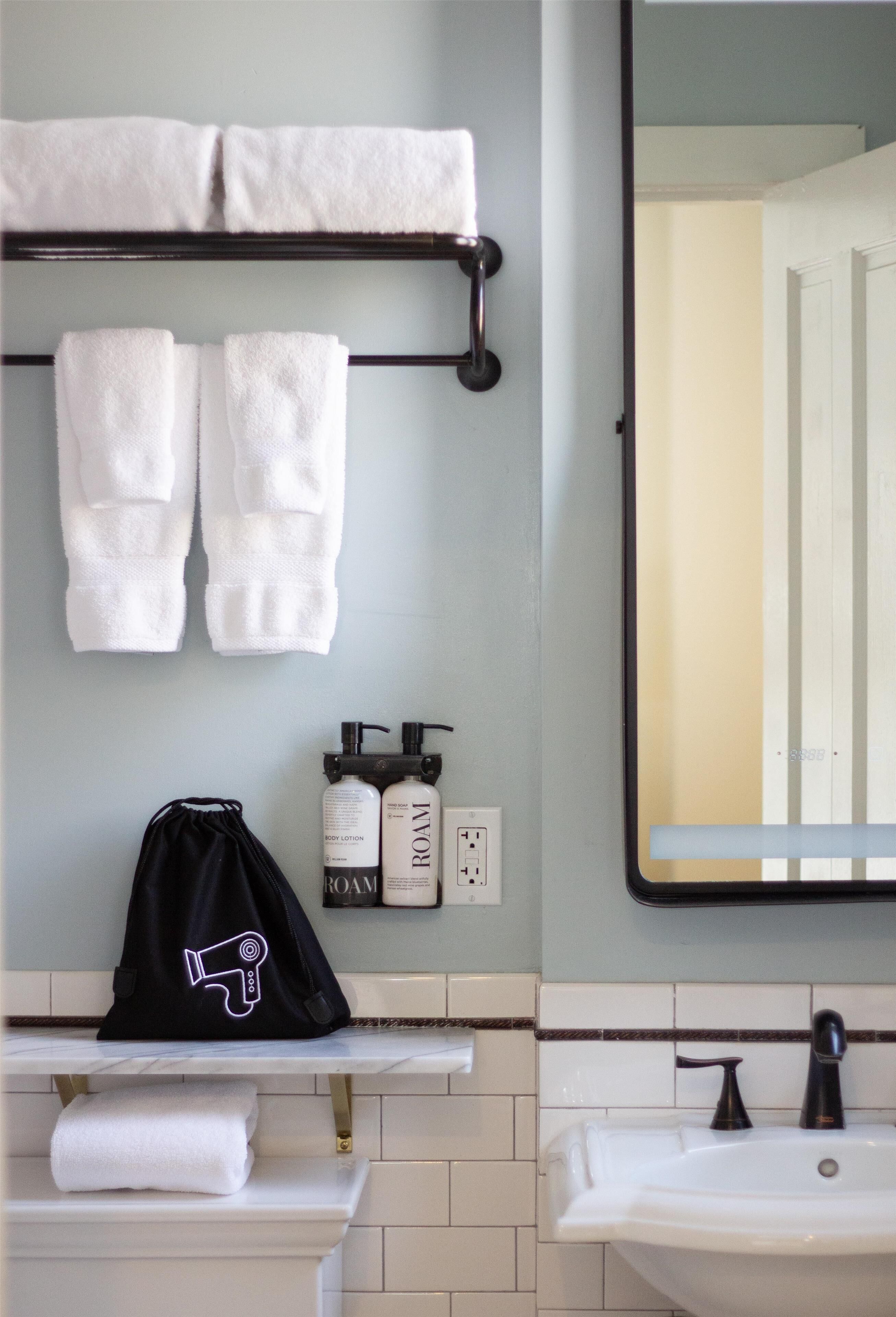 Une salle de bain avec un porte-serviettes sur lequel sont posés deux serviettes blanches, un sac noir à cordon de serrage et deux flacons de lotion pour le corps de la marque Roam.