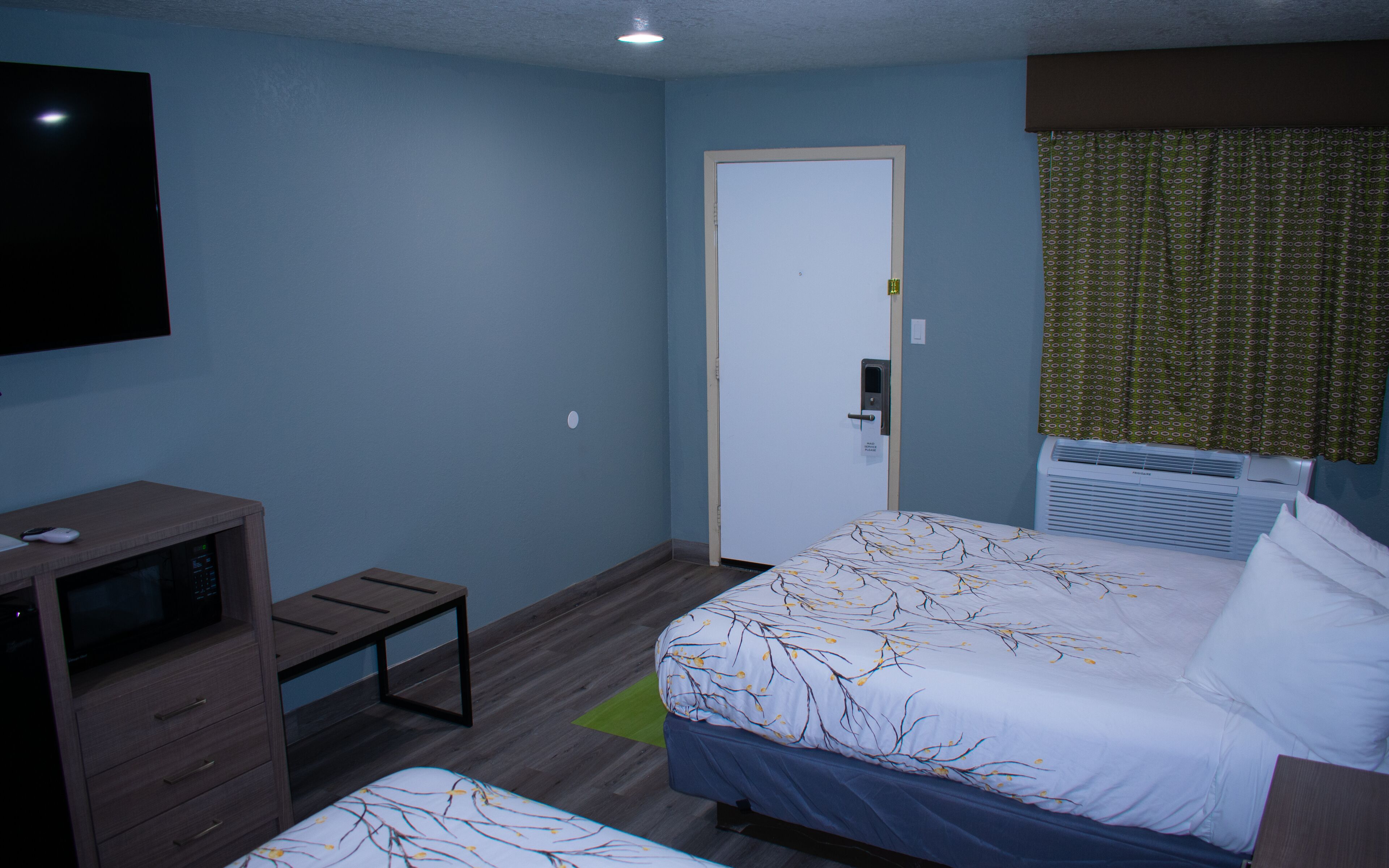 A hotel room with a bed, a desk with a computer, a TV, and a door.