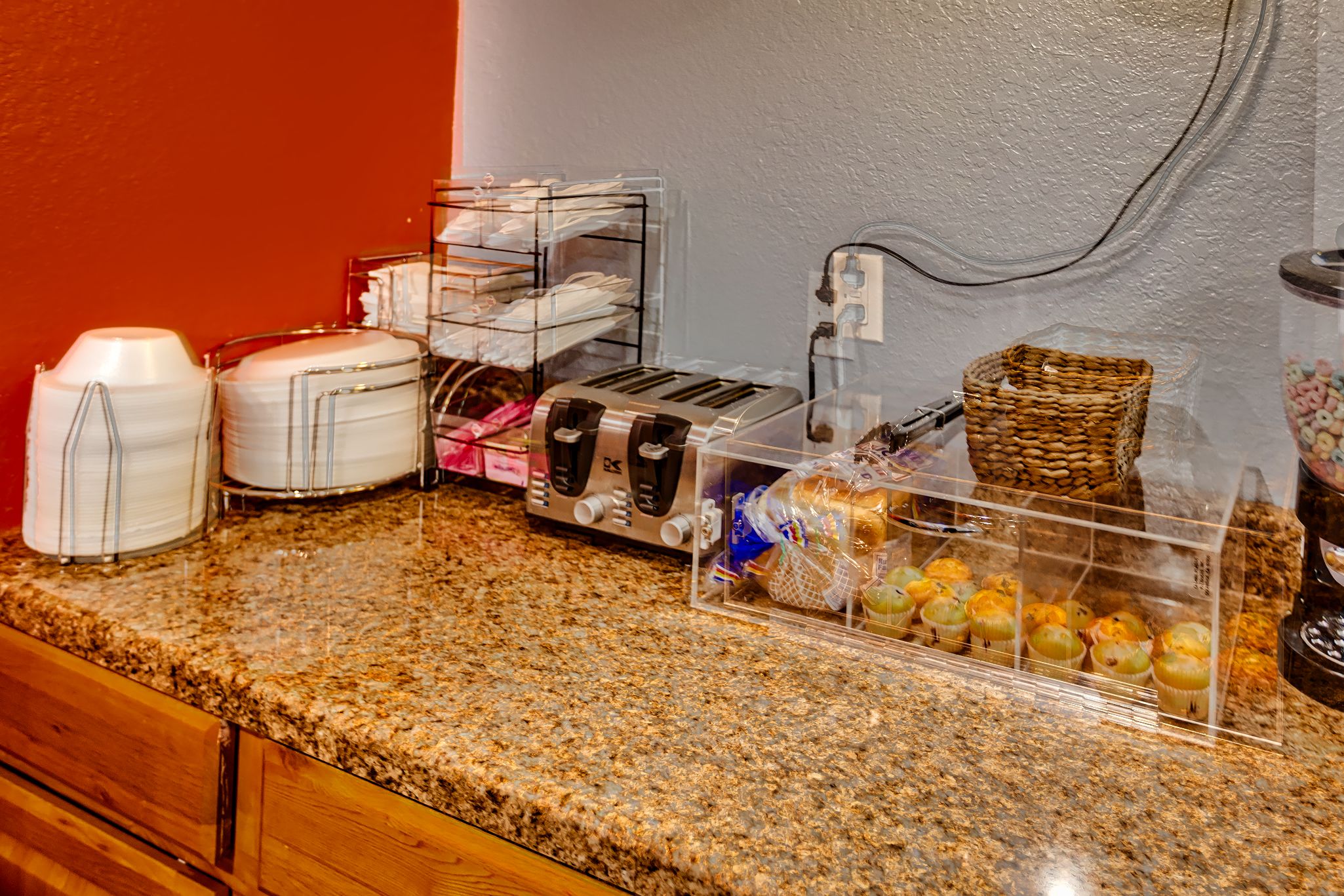 A kitchen counter with a toaster, coffee maker, and a display case with muffins.