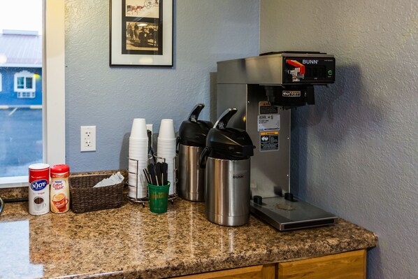 Un espacio tipo cocina con cafetera, tazas desechables, una cesta y otro fabricante de café.