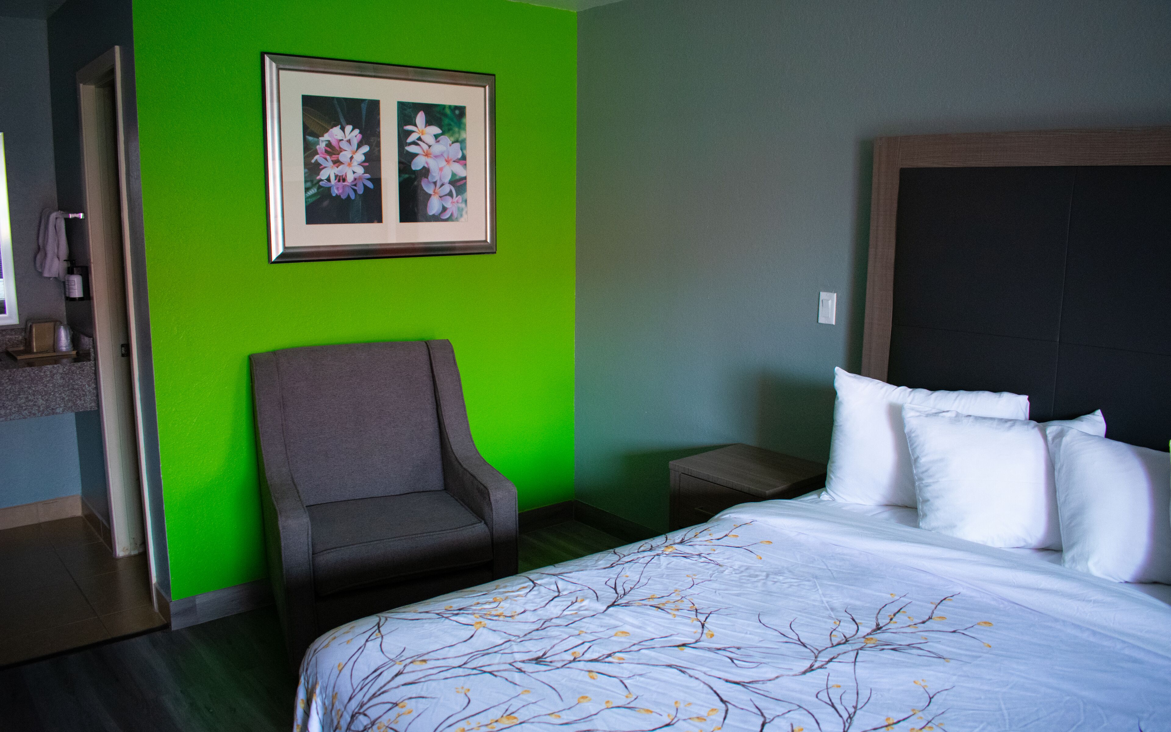 Una habitación de hotel con una cama, una silla, una mesita de noche y un cuadro en la pared.