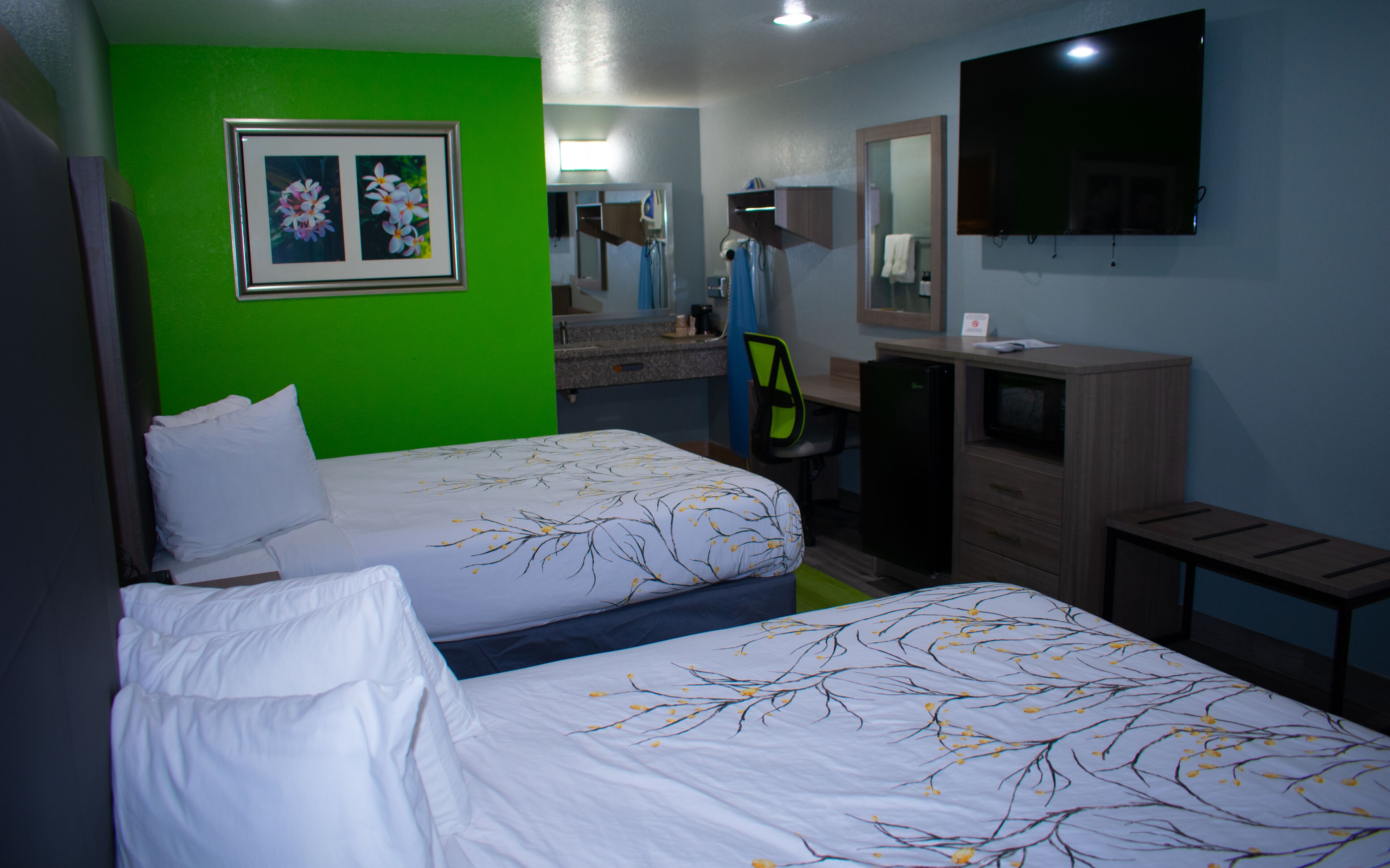 A hotel room with two beds, a desk, a chair, a TV, and a bathroom visible in the background.