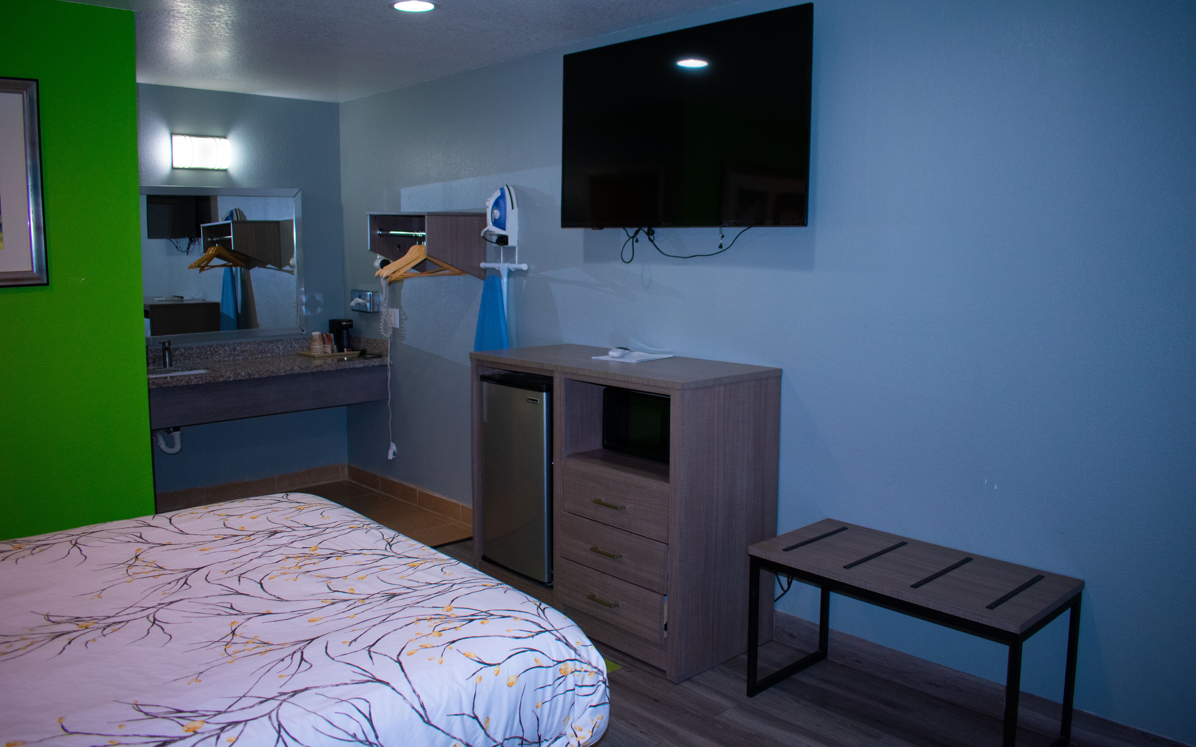 A hotel room with a bed, a desk, a mirror, a TV, and a bathroom.