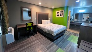 A hotel room with a bed, a desk, a chair, a mirror, and a bathroom area.