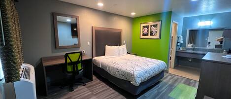 A hotel room with a bed, a desk, a chair, a mirror, and a bathroom area.