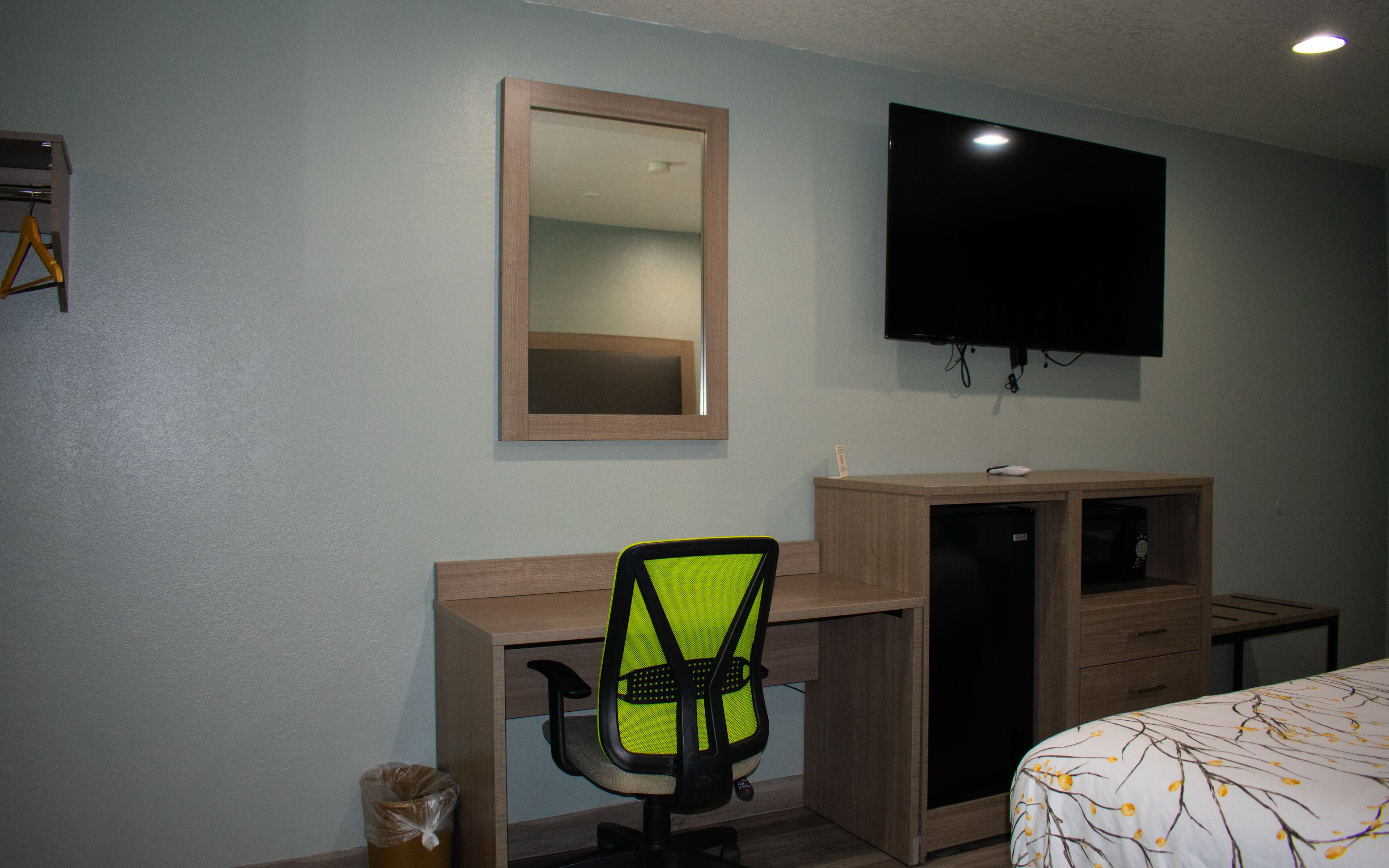 Un dormitorio con cama, escritorio, silla, televisor y espejo.