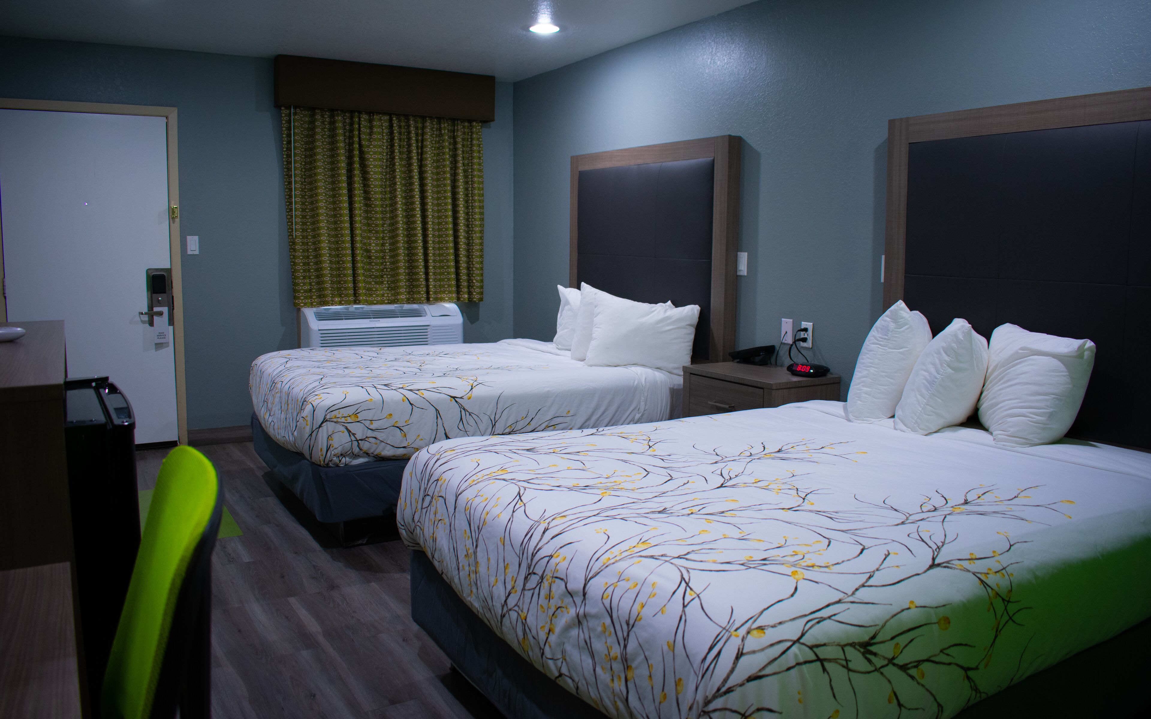 Une chambre d’hôtel avec deux lits, un bureau, une chaise, un appareil de climatisation et une horloge.