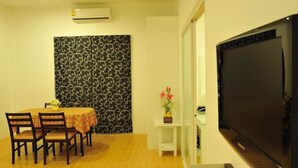 A dining area with a table and chairs, a patterned wall, a small table with a vase, and a large flat-screen TV. - Boutique Guesthouse by Clearhouse (Kamala)