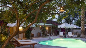 Une piscine avec des chaises longues, un espace de détente couvert et un bâtiment doté d’un toit en tuiles.
