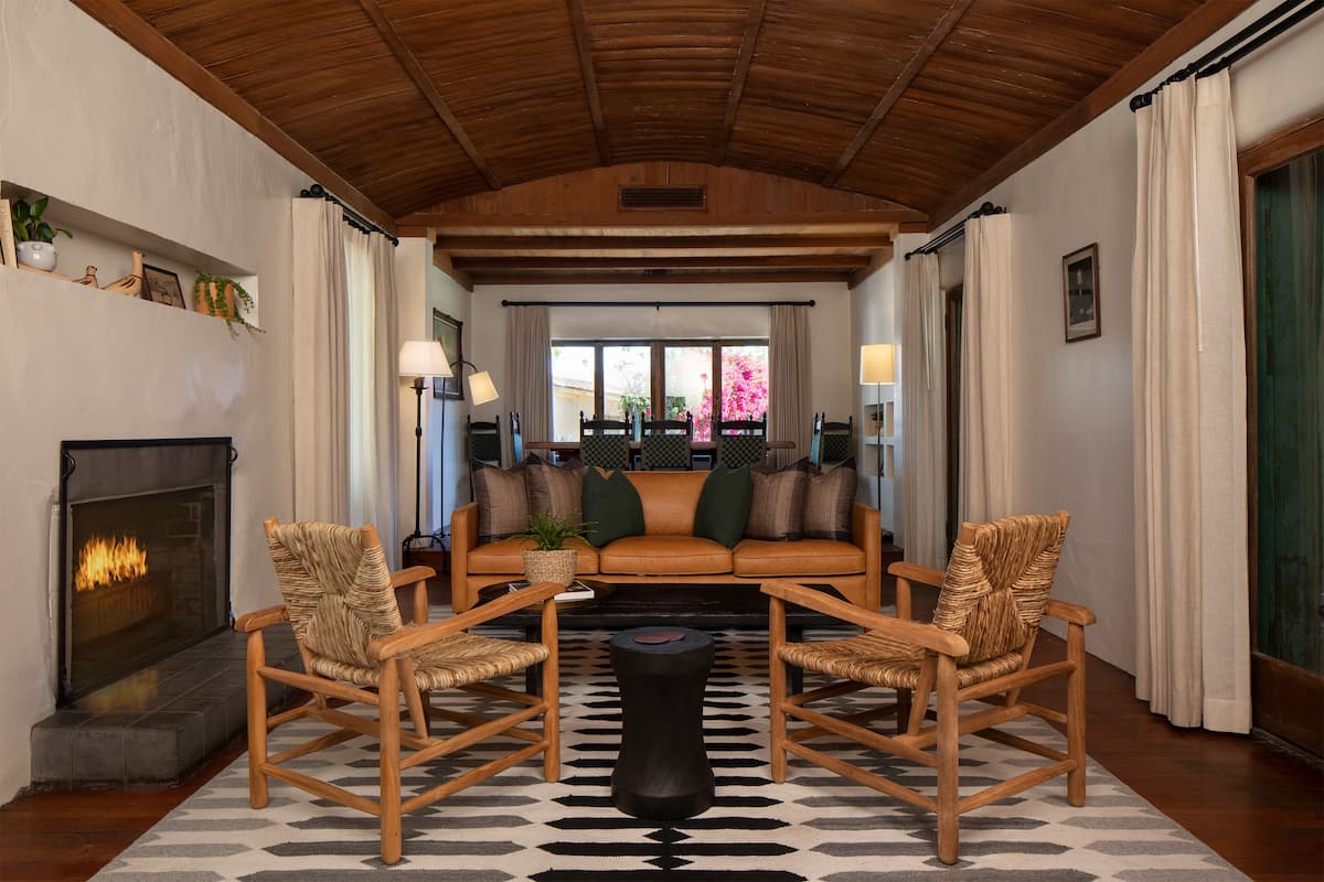 A cozy living room with a fireplace, a sofa, and two wicker chairs.