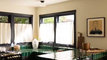 A kitchen with a green tiled backsplash, a stove, a sink, and a window with curtains.