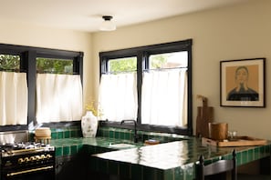 A kitchen with a green tiled backsplash, a stove, a sink, and a window with curtains.