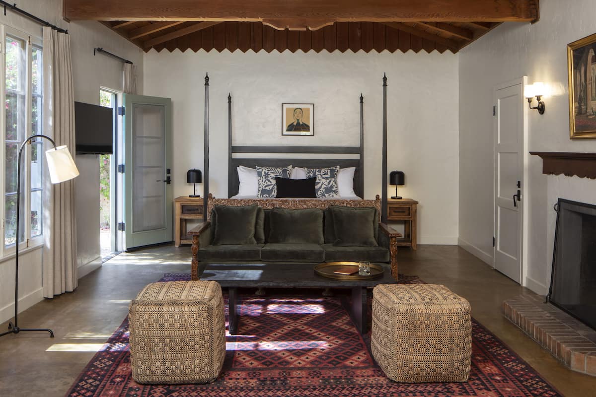 A cozy room with a four-poster bed, a fireplace, and a large window with curtains.