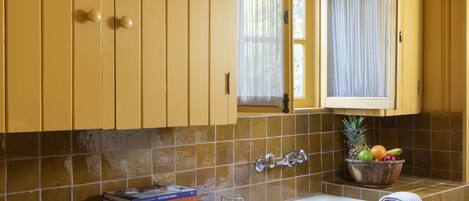A kitchen with yellow cabinets, a tiled backsplash, a sink, and a window with curtains.