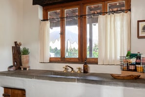A kitchen with a stone countertop, a wooden window frame, and a view of greenery outside.